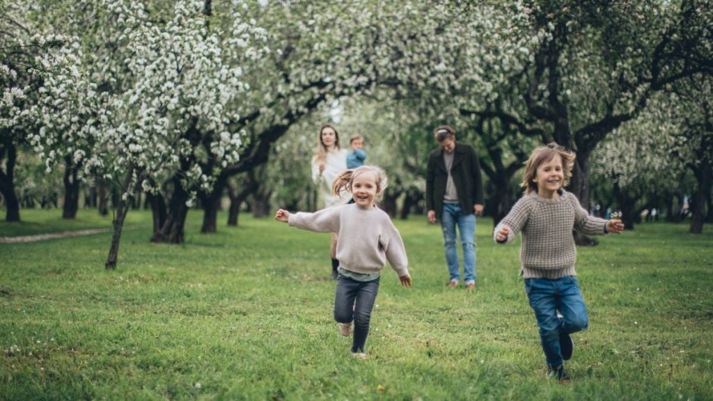 A happy family running and playing among blooming trees in a lush green park during spring.