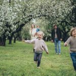 A happy family running and playing among blooming trees in a lush green park during spring.