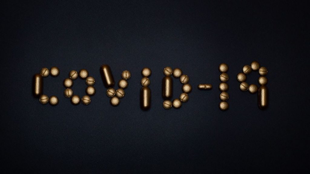 Artistic representation of COVID-19 using golden pills on a black background, symbolizing healthcare and treatments.