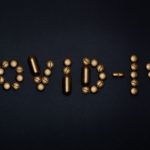 Artistic representation of COVID-19 using golden pills on a black background, symbolizing healthcare and treatments.